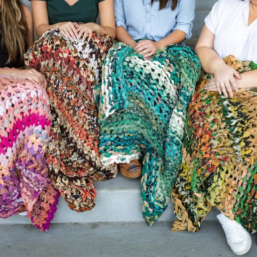 Group of women sitting together on stairs with vibrant chunky knit blankets in various colors, symbolizing unity, ethical fashion, and freedom through handmade products.